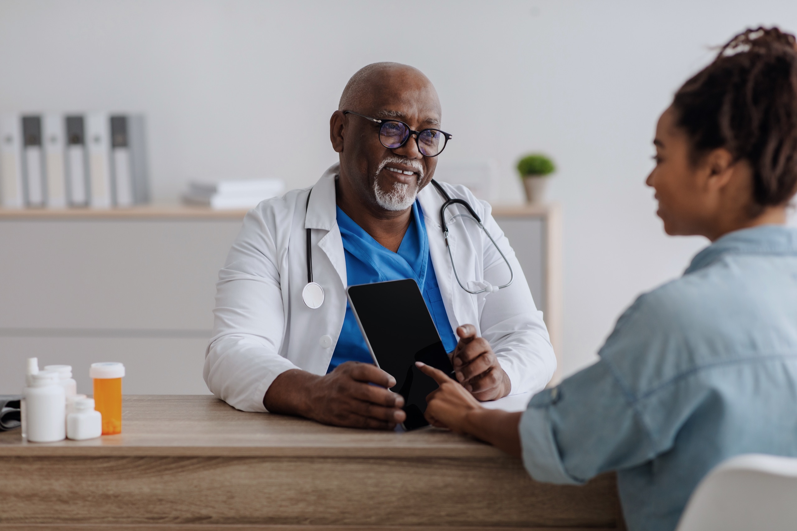 A physician reviewing records on a tablet with a patient, keeping the clinical judgment with the clinician.