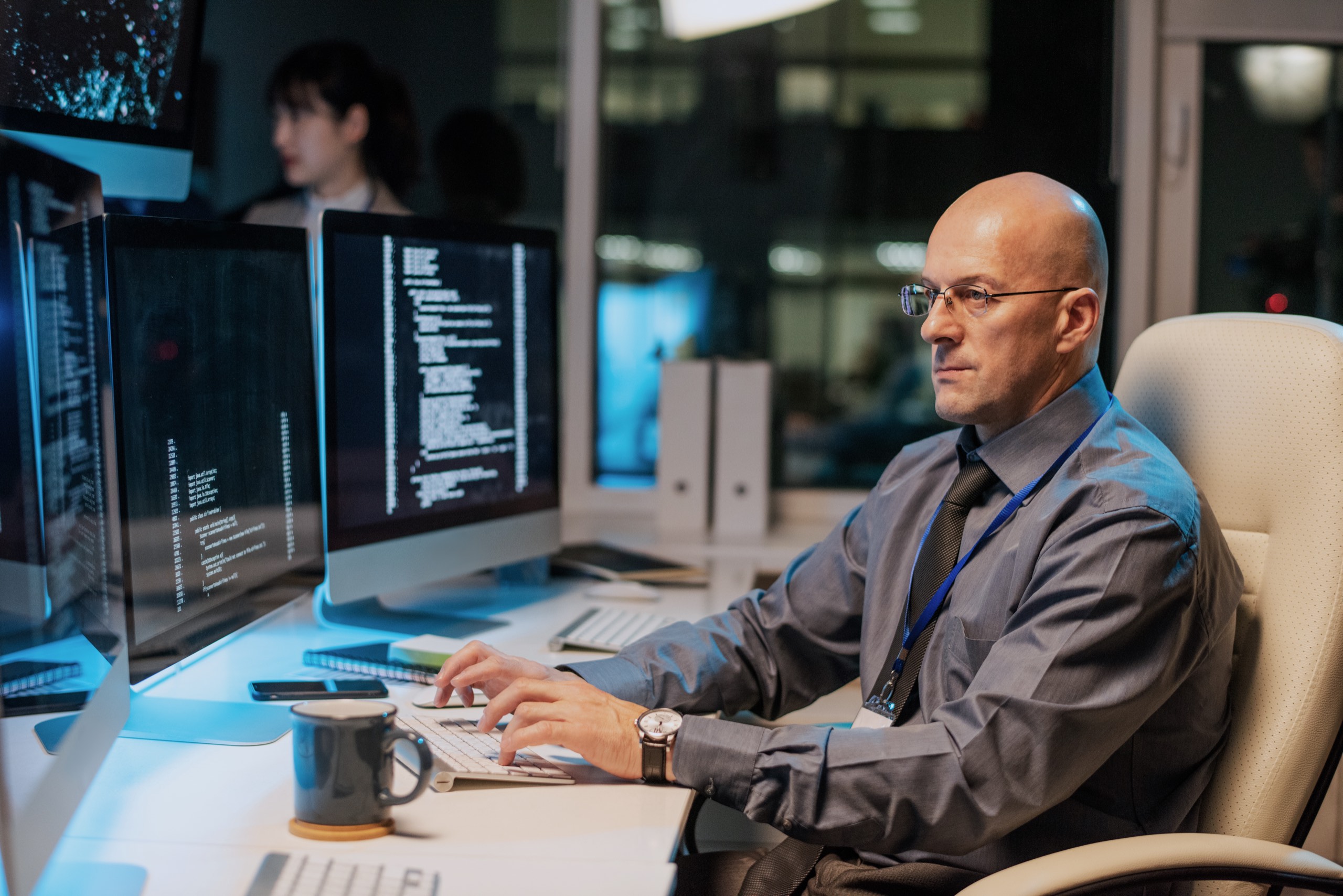 A professional reviewing system output across multiple screens in a low-lit operations room.